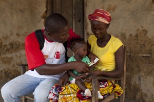 Emmanuel, a Save the Children Community Health Volunteer,  undertakes a health check on Patience, 8 months, who is sitting on her mother, Elizabeth's lap.  Credit:  Martin Webb/Save the Children.